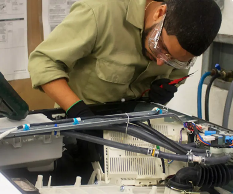 Technician in safety glasses repairing an opened dishwasher on a workbench